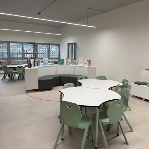 Zona infantil de biblioteca con mesas en forma de flor, sillas verdes y mueble circular para libros