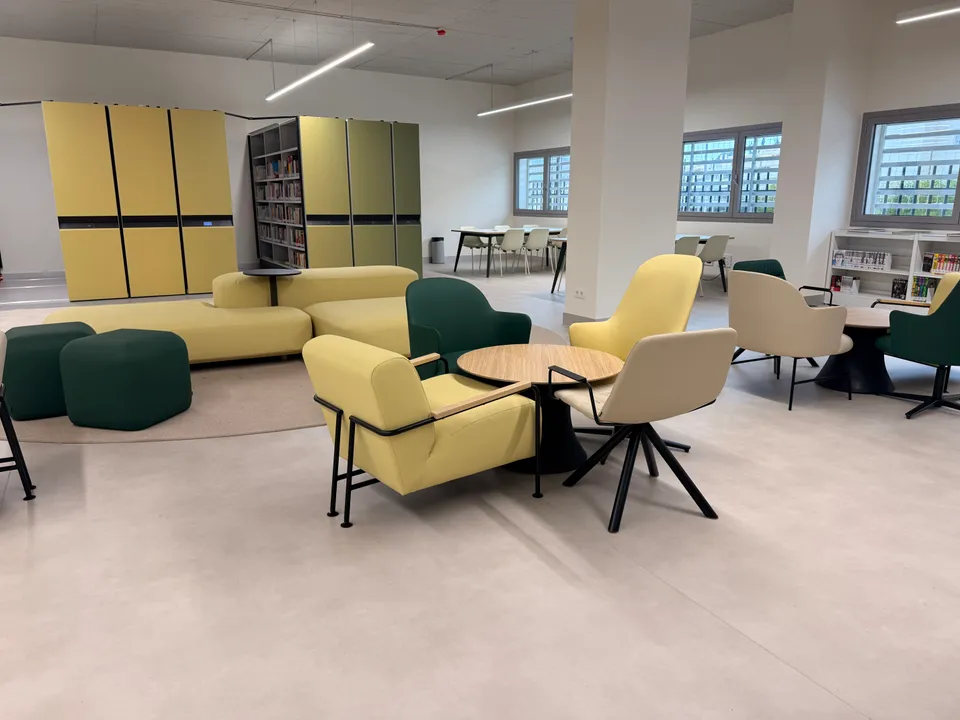 Zona de lectura con sillones en mostaza y verde, pufs y estanterías correderas de colores