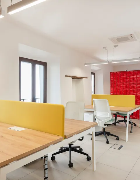 Puestos de coworking con paneles amarillos junto a la ventana