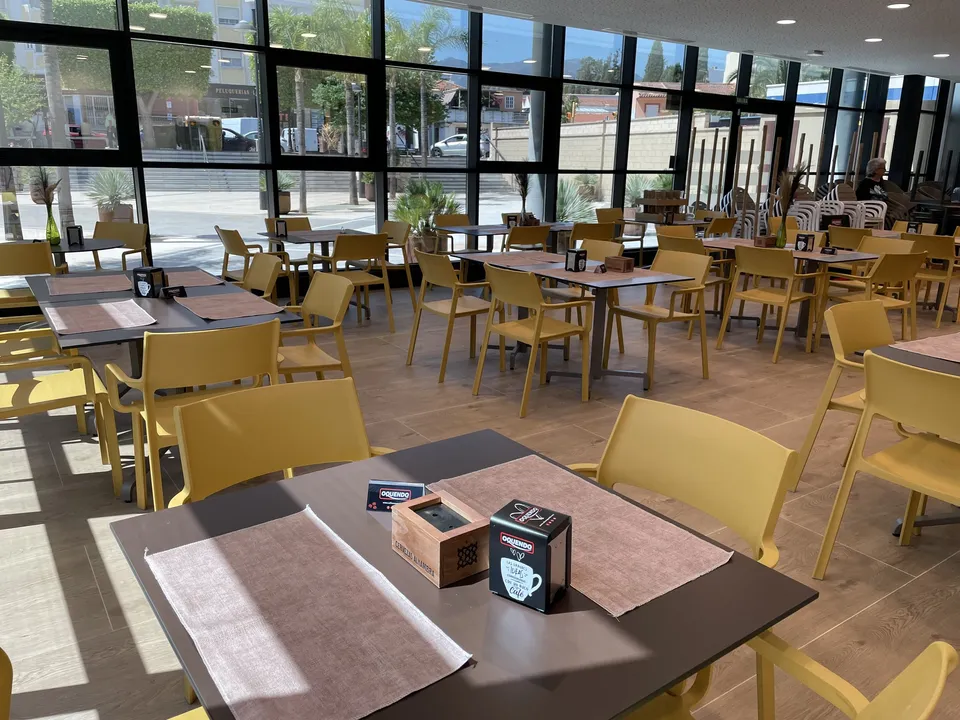 Comedor con mesas y sillas mostaza junto a ventanales